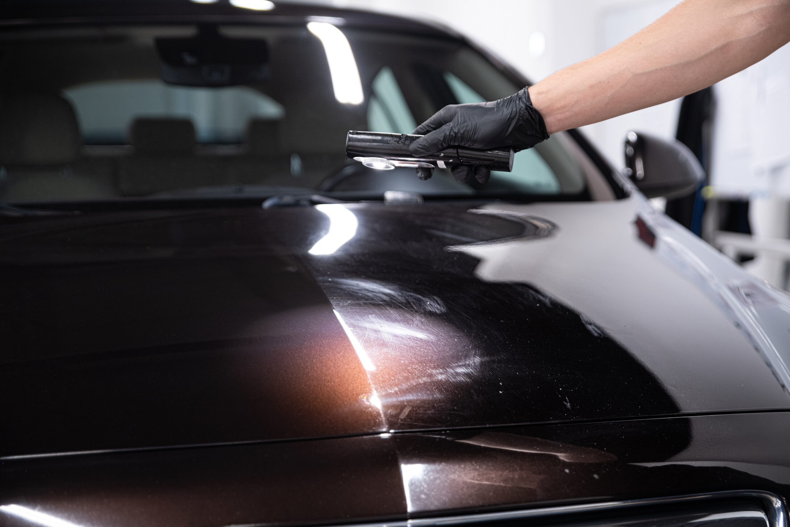 An auto detailing expert shines a light on the hood of a sports car, revealing scratches and paint swirls